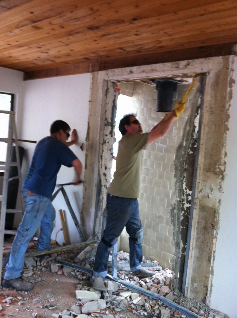 Two workmen tearing out tile around fireplace. 