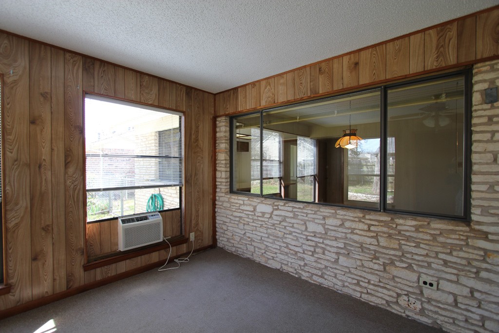 View of old sun room addition with window AC, gas heater, outdoor carpet, cigarette burns.