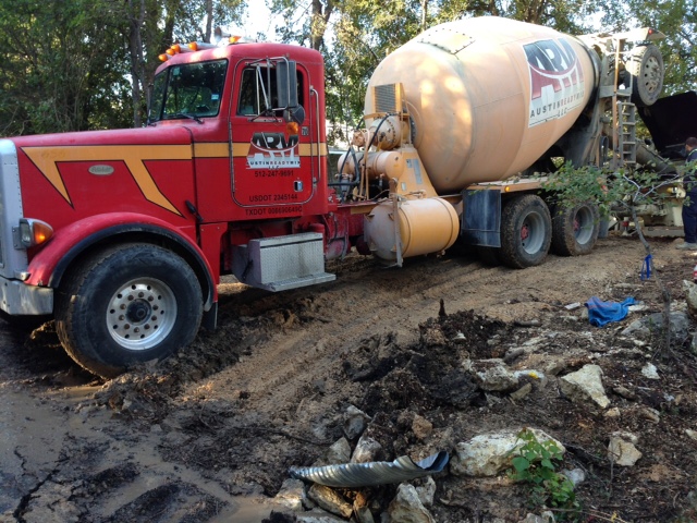 Heavy concrete truck spinning wheels in mud during foundation pour.