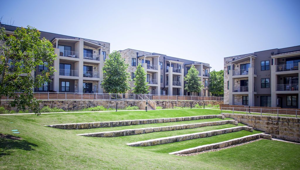 View of amphitheater with green grass and stone seating on Denizen Condominium grounds.