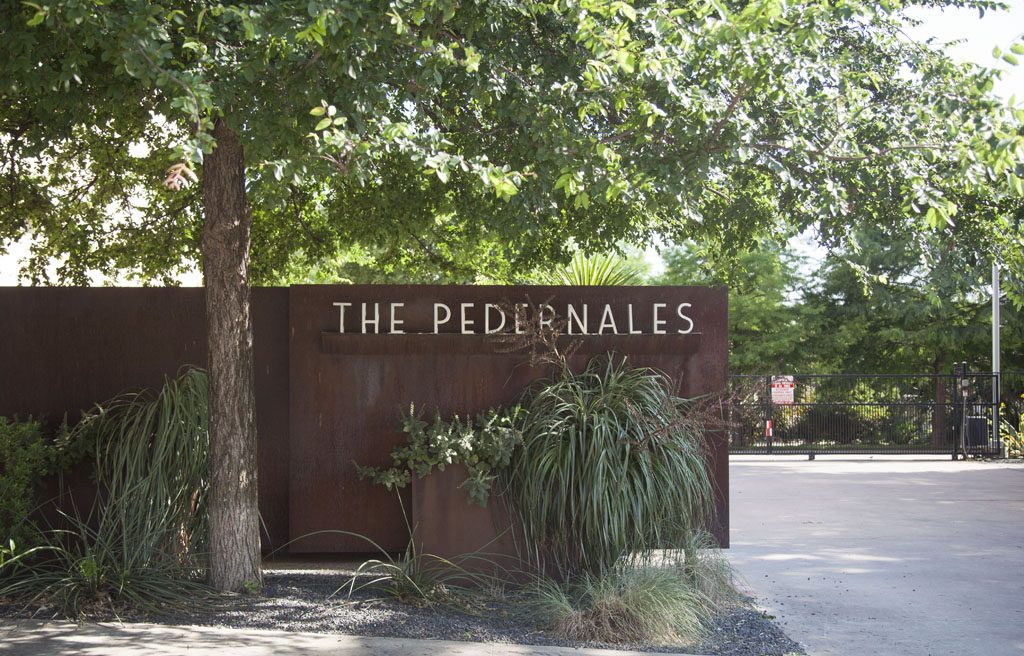 Pedernales Lofts iron gated entrance showing condo name under shade trees in East Austin.