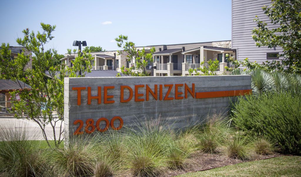 The Denizen Condos entrance sign is board formed concrete with orange letters.