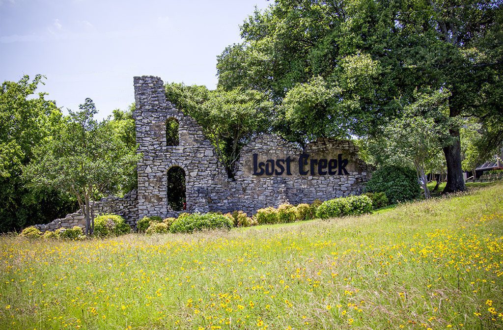 Lost Creek neighborhood in Westlake area has old stone entrance sign set in field of wildflowers.