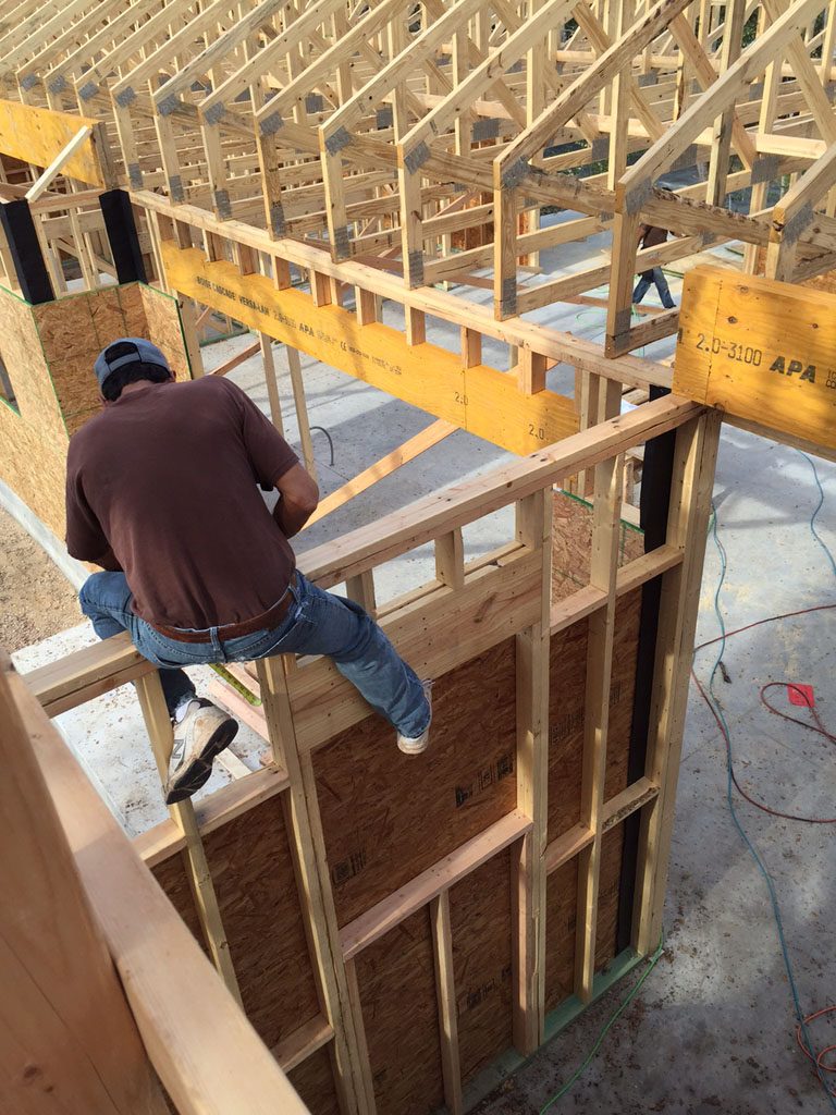 Carpenter is shown working a a wall during framing of modern farmhouse.