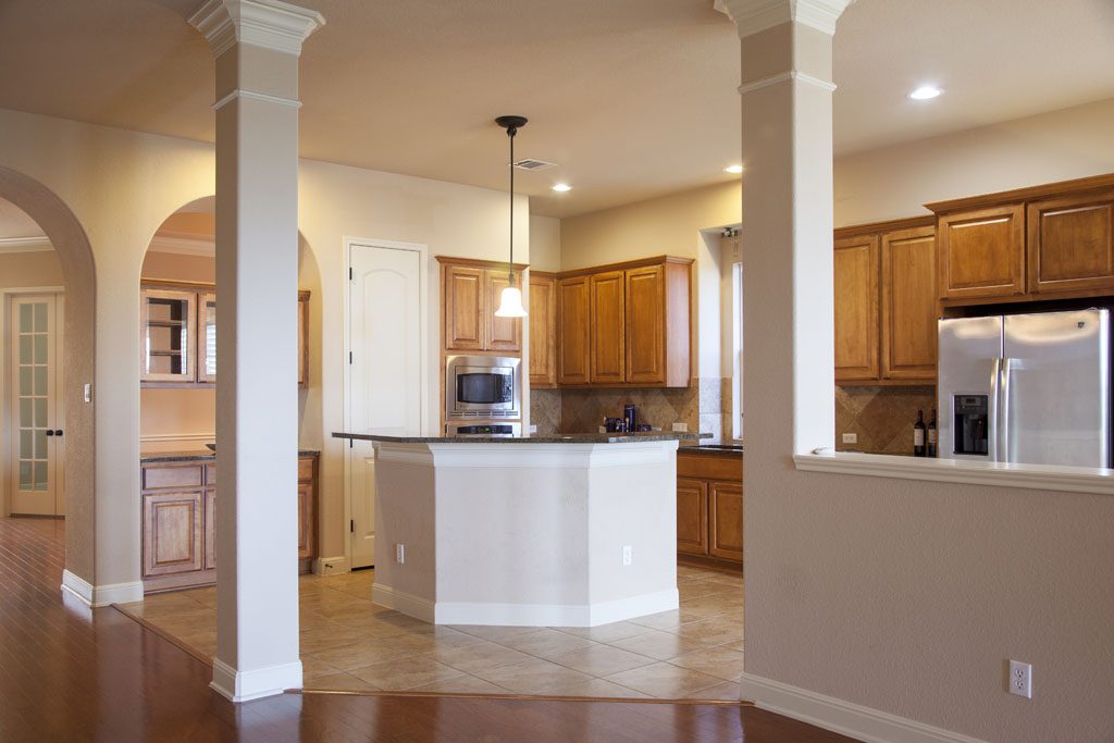Wide view of kitchen showing columns, tile floor, central island.